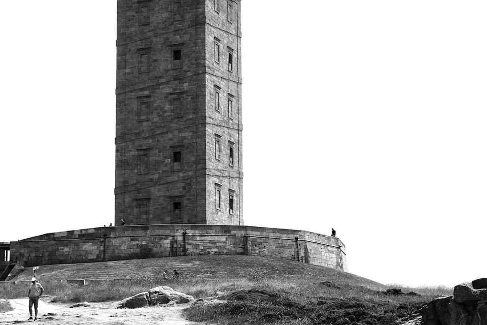 La Torre de Hércules de A Coruña vista desde el paseo, con una persona caminando cerca