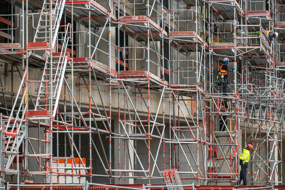 Operario de pie en un andamio delante de la fachada de un edificio en obras